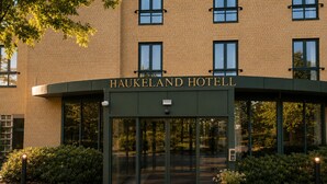 The Haukeland Hotel entrance with a glass door, a nameplate, and a potted plant. - Haukeland Hotell (Bergen)
