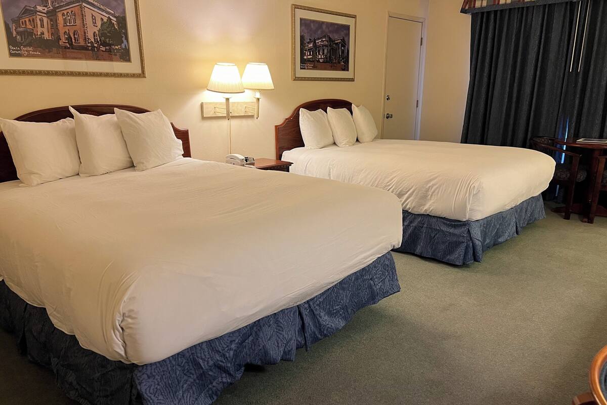 A hotel room with two large beds, a nightstand with a lamp, and a door with a curtain.