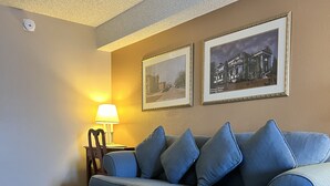 A living room with a sofa, a small round table, a lamp, and two framed pictures on the wall. - Hardman House Inn & Suites (Carson City)