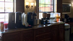 A kitchen area with a coffee station, a window with blinds, and a wall-mounted light fixture. - Hardman House Inn & Suites (Carson City)