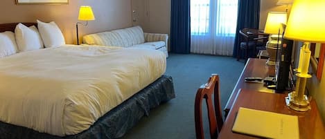A hotel room with a large bed, a desk with a lamp, and a chair.
