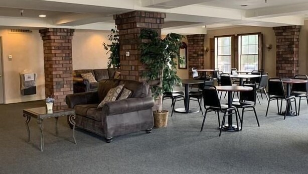 A spacious indoor area with a brick fireplace, a sofa, and a dining area with tables and chairs. - Hardman House Inn & Suites (Carson City)