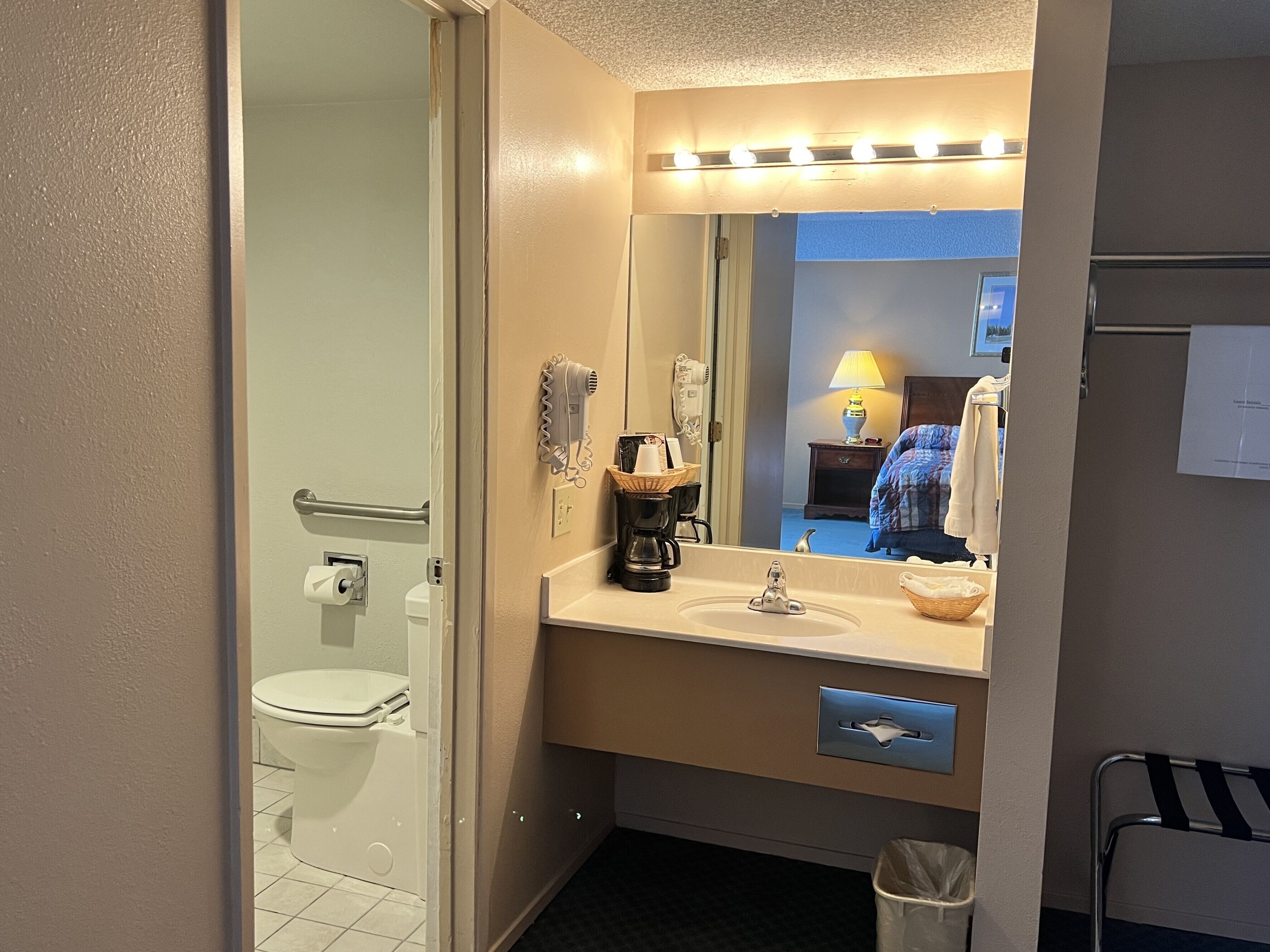 A bathroom with a toilet, sink, and mirror. There is a hairdryer and a basket on the counter.