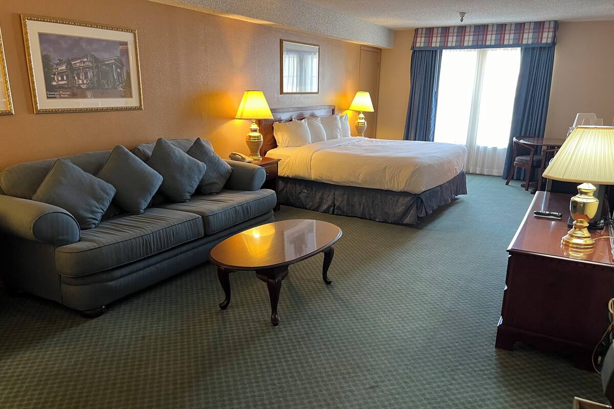 A hotel room with a sofa, a bed, a small table, lamps, and a framed picture on the wall.