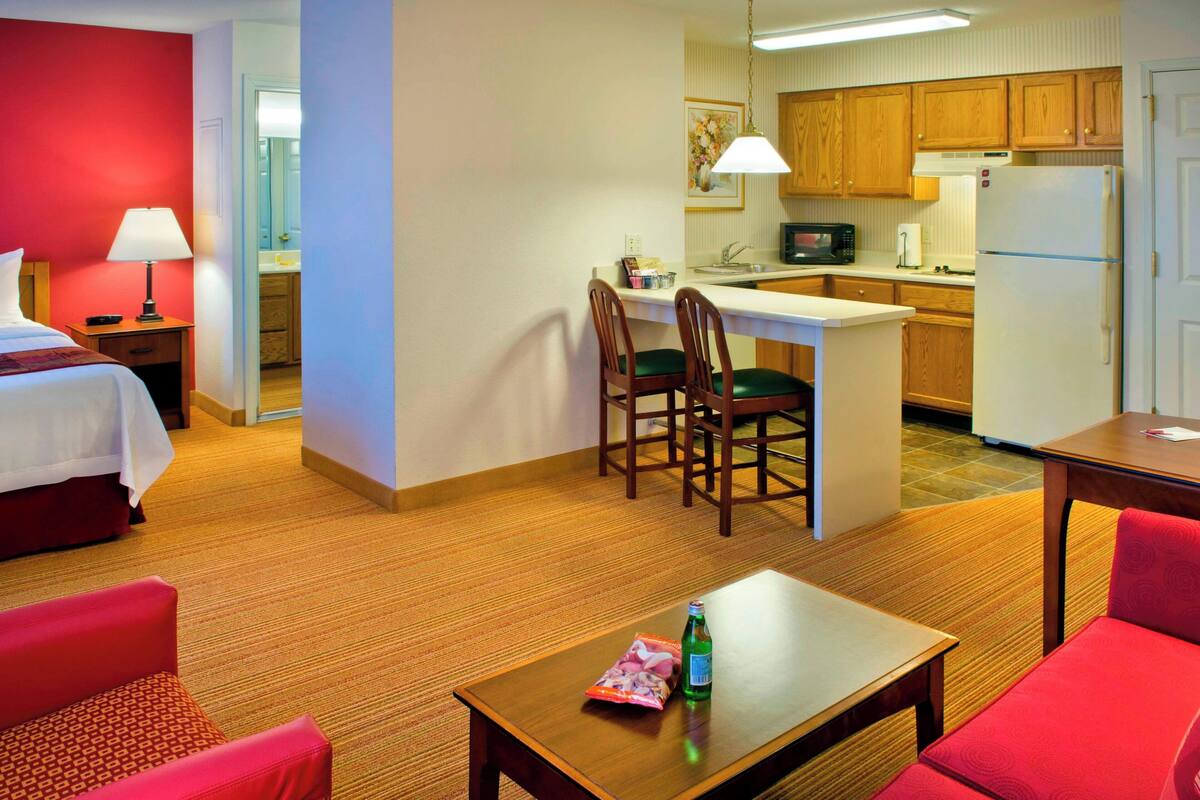 A hotel room with a bed, a small kitchenette, a dining area with a table and chairs, and a separate living area with a sofa.