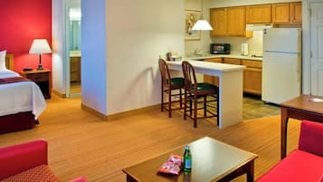 A hotel room with a bed, a small kitchenette, a dining area with a table and chairs, and a separate living area with a sofa.