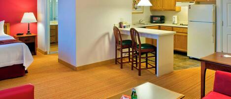 Habitación de hotel con cama, kitchenette pequeño, zona de comedor con mesa y sillas, y sala de estar separada con sofá.