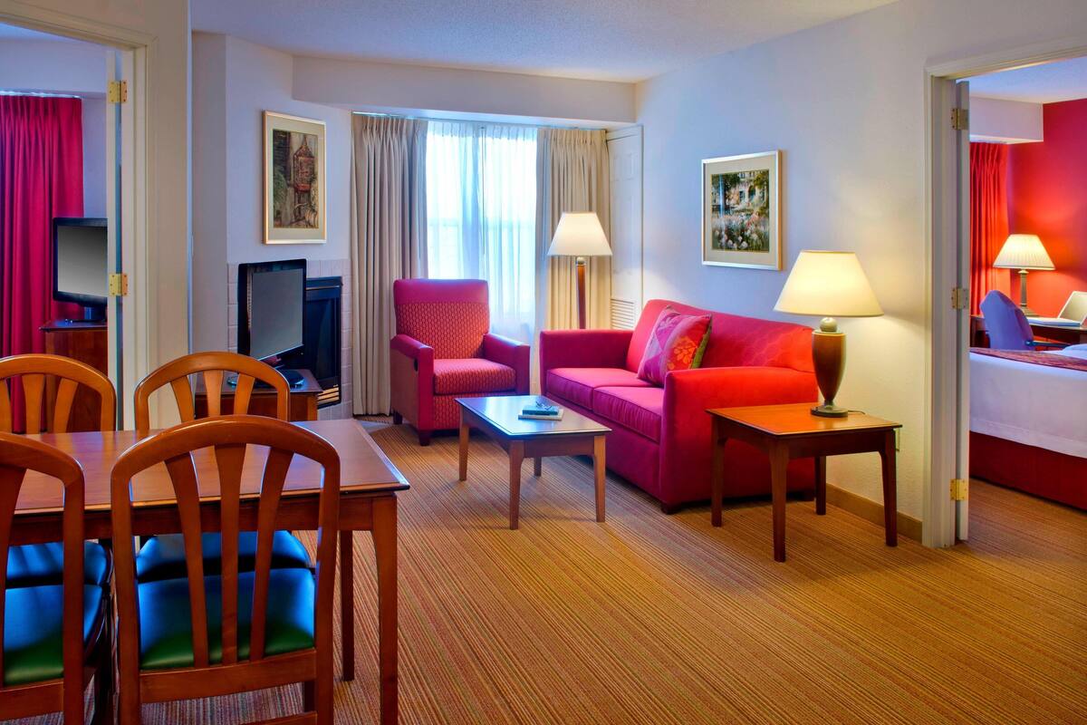 A hotel room with a dining area, a red sofa, a TV, and a fireplace.