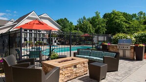 Une terrasse extérieure aménagée avec des meubles en osier, un foyer en pierre, une piscine et un barbecue.