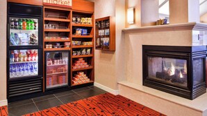 Un hall d’hôtel équipé d’un réfrigérateur pour les boissons, d’étagères remplies d’en-cas, d’une cheminée et d’un panneau indiquant « l’épicerie ».