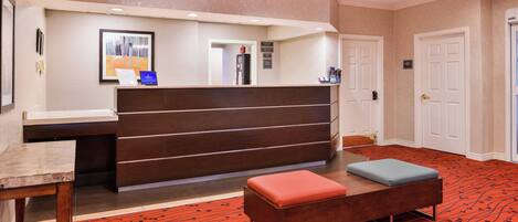 A reception area with a wooden desk, a bench with a red cushion, and a patterned carpet.