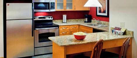 A kitchen with a refrigerator, microwave, oven, granite countertop, wooden cabinets, and a dining area with chairs.