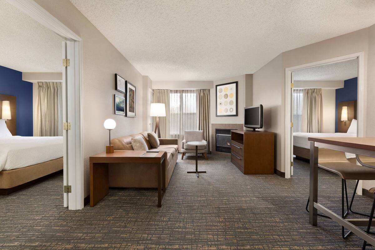 A hotel room with a bed, a sofa, a desk, a chair, a TV, and a fireplace.