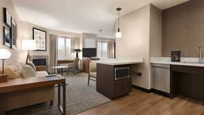 Ein kompaktes Hotelzimmer mit Küchenzeile, einer Couch, einem Schreibtisch und einem Fernseher.