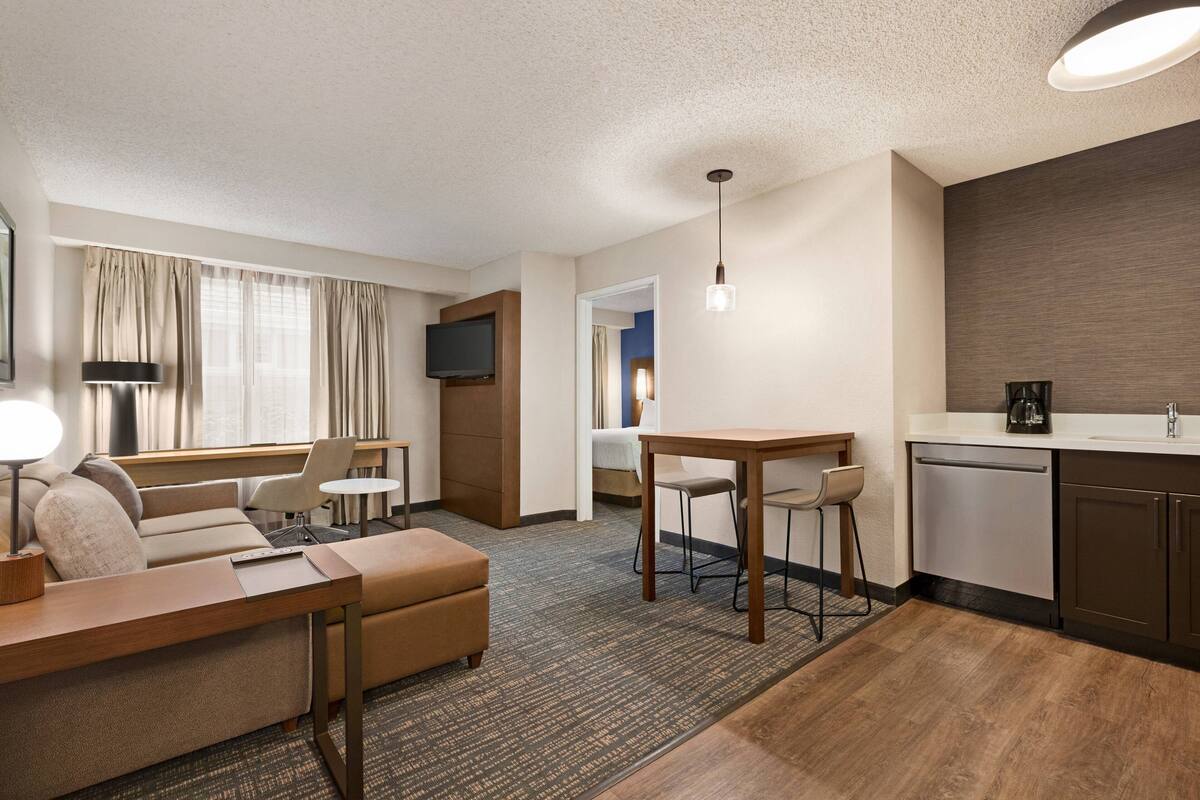 A hotel room with a living area, kitchenette, and a small dining table.