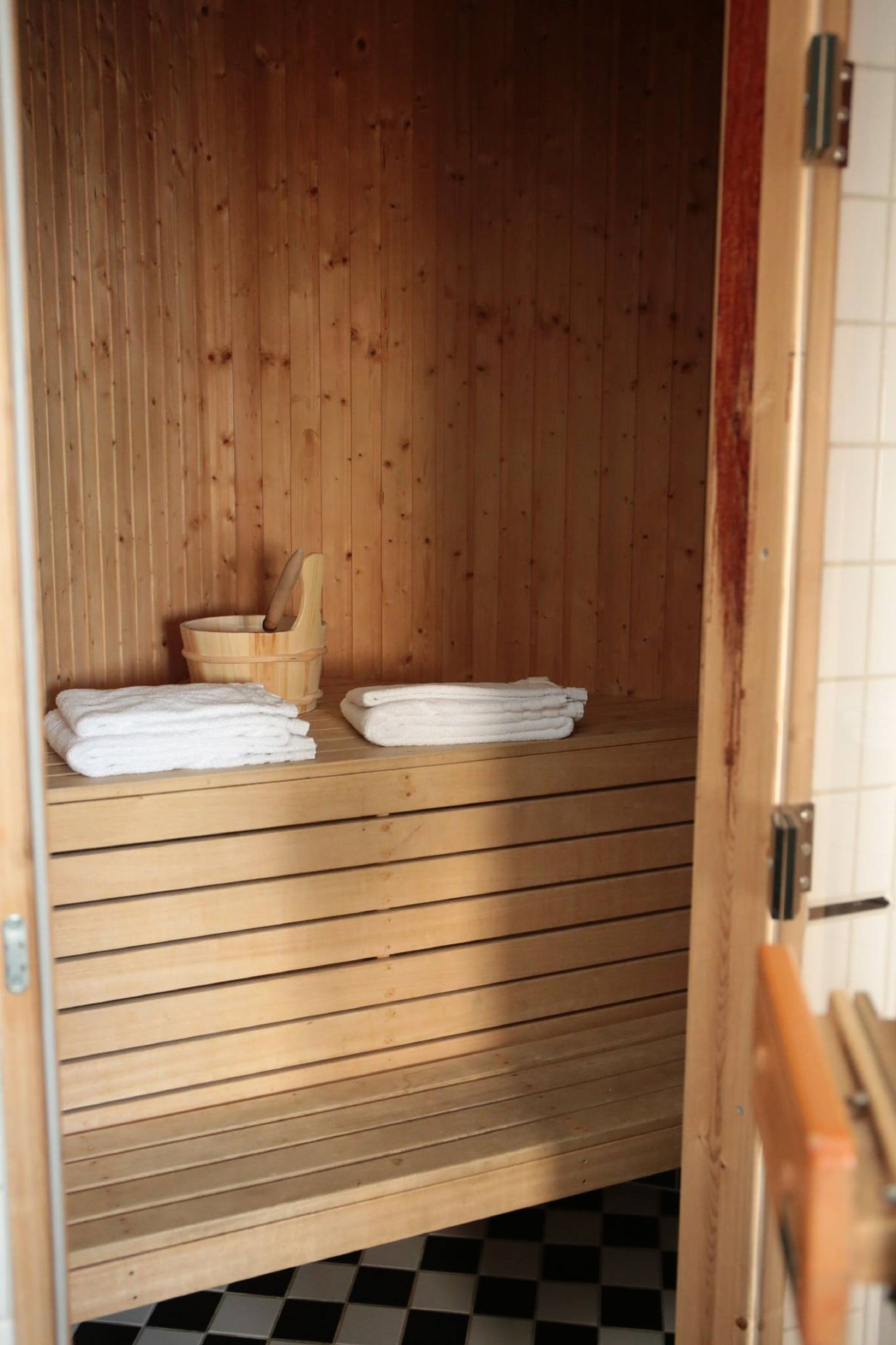 Una sauna de madera con piso a cuadros, un banco de madera y un balde de madera.
