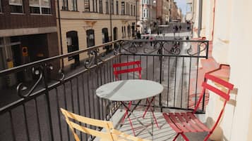 Un balcó amb taula i cadires, amb vista a un carrer amb edificis i gent.