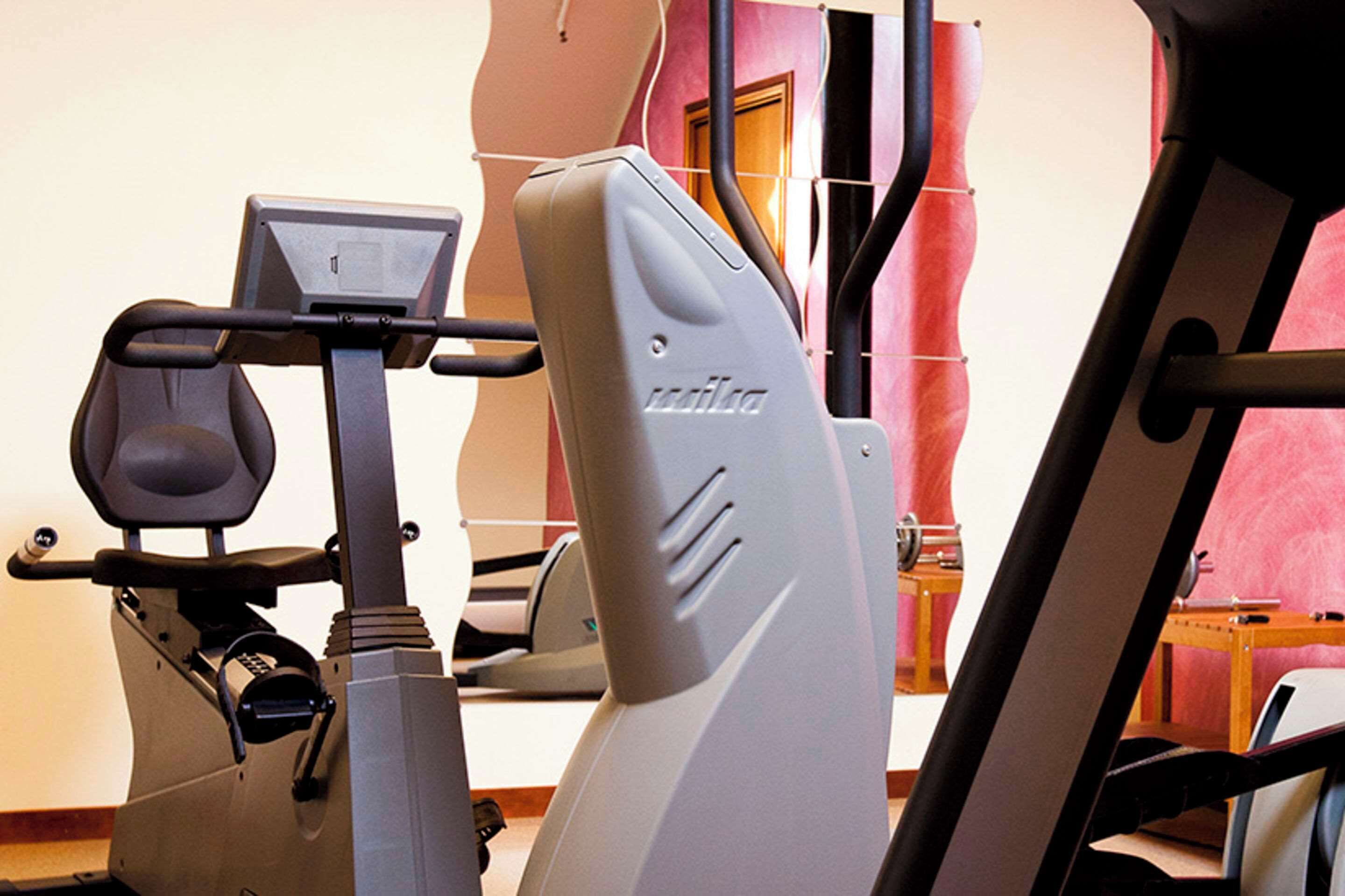 A stationary bike and a treadmill in a room with a pink wall and a door in the background.