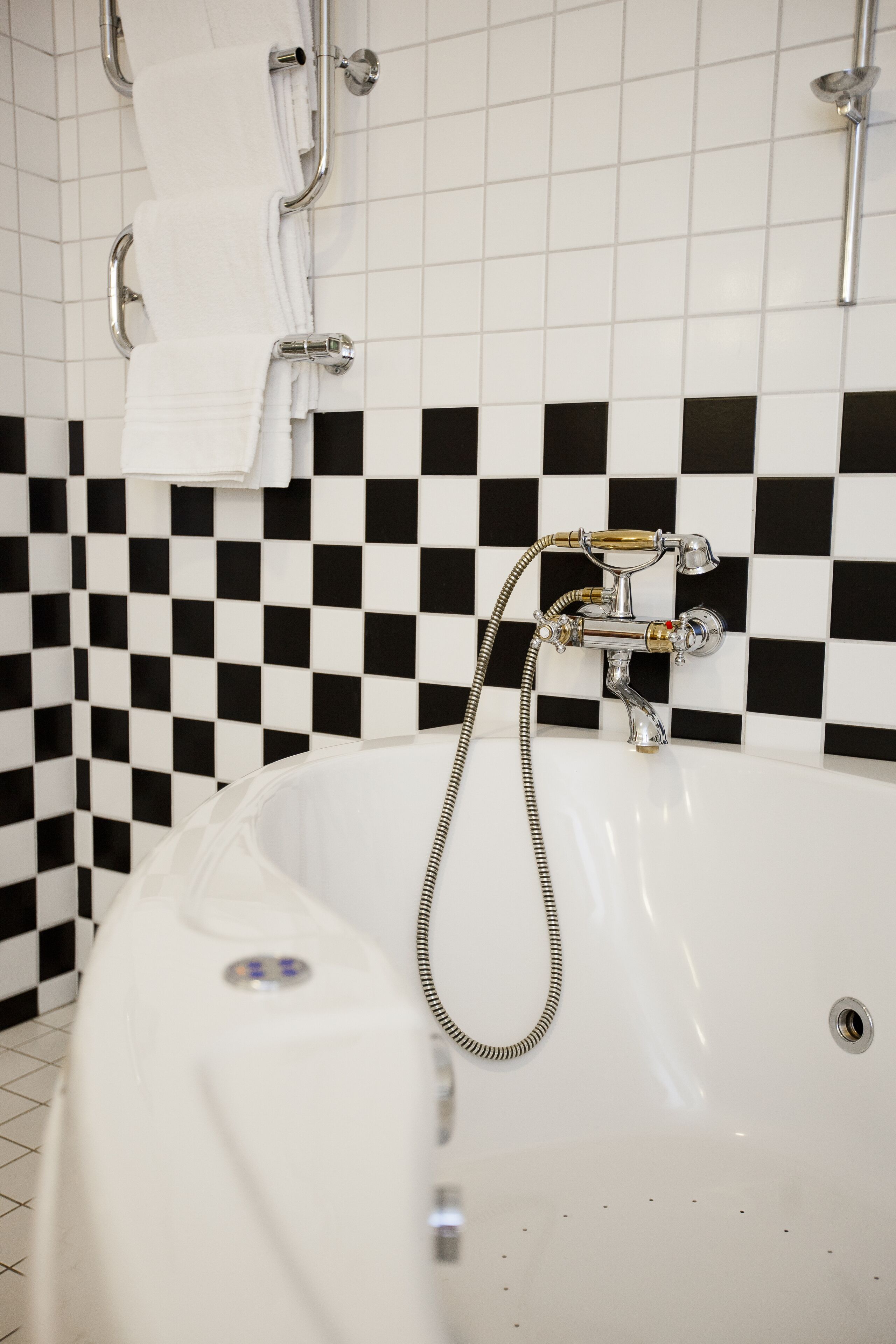 A bathroom with a checkered black and white tiled wall, a white bathtub, and a shower with chrome fixtures.