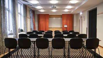 Un salón de conferencias con piso a cuadros, sillas negras, una mesa larga y una pantalla para proyector.