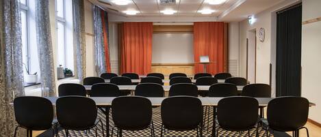 Un salón de conferencias con piso a cuadros, sillas negras, una mesa larga y una pantalla para proyector.