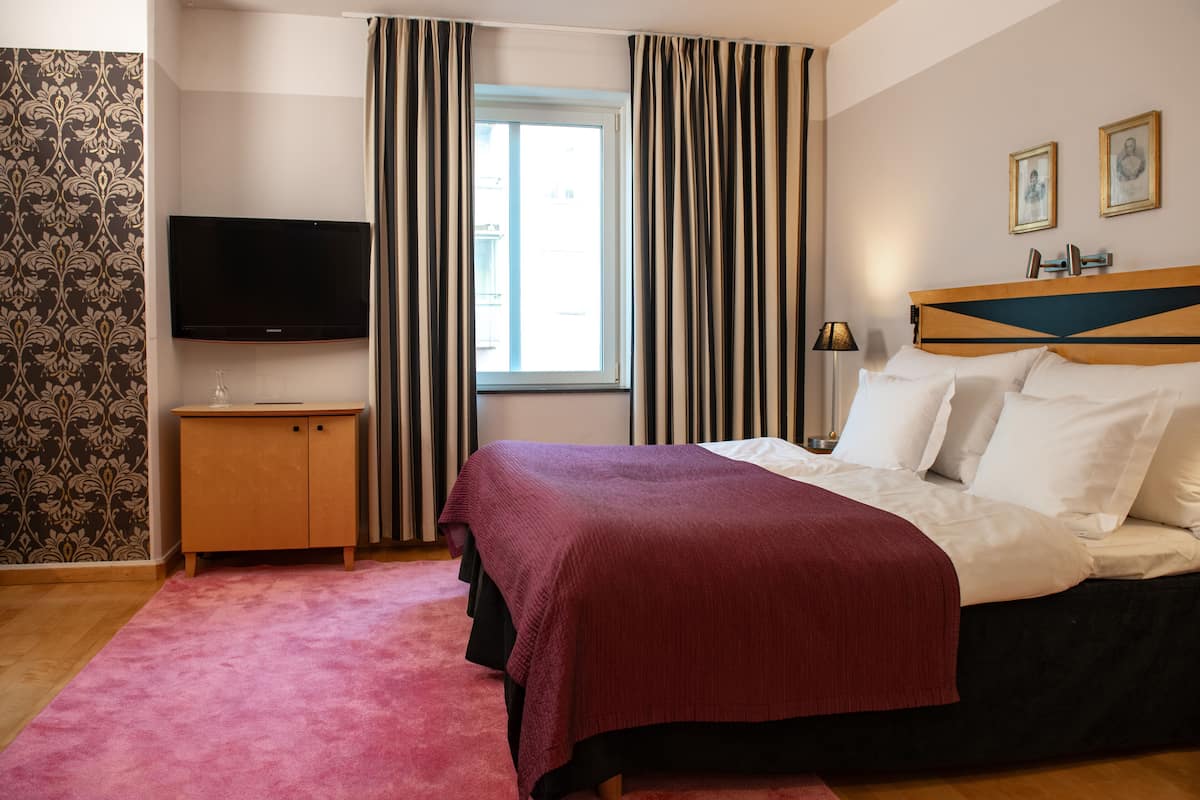 A hotel room with a bed, a television, a wardrobe, and a window with curtains.