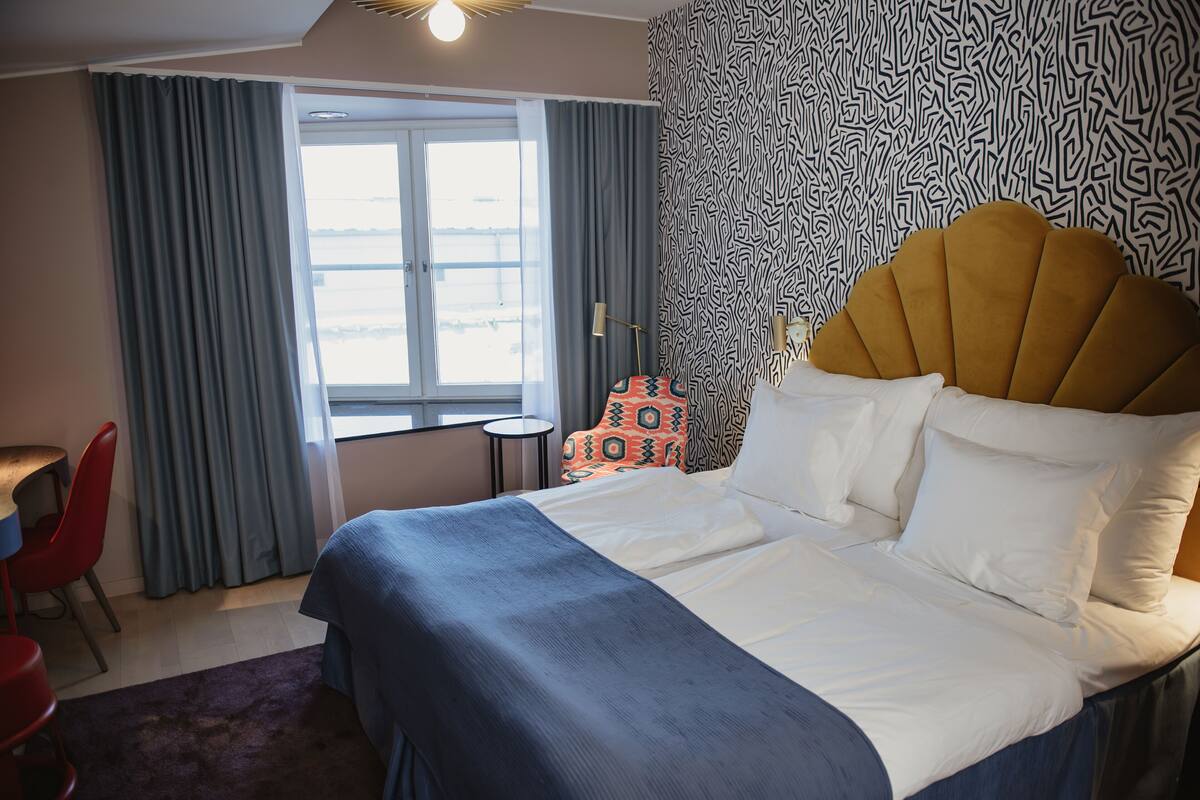 A hotel room with a large bed, a desk, a chair, and a view of the outdoors through a window.