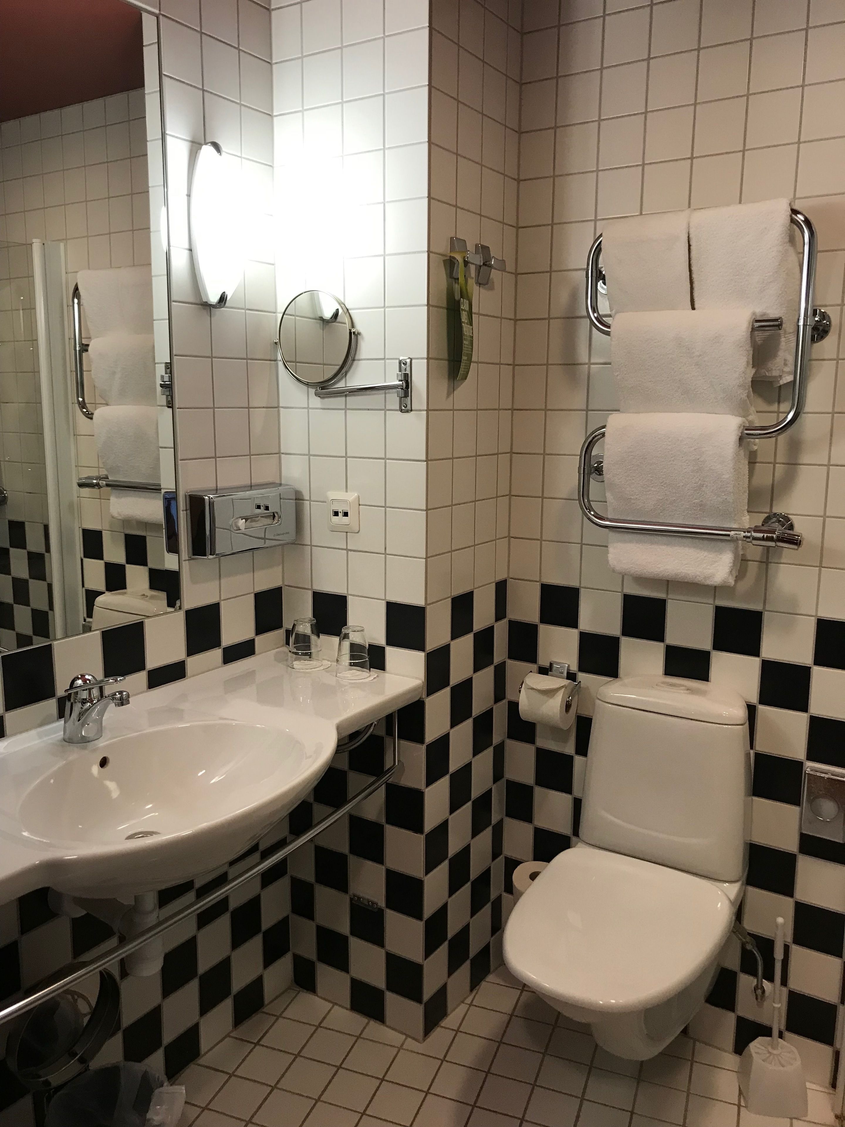 Et badeværelse med vask, spejl, toilet og håndklædeholdere.