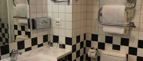 Et badeværelse med vask, spejl, toilet og håndklædeholdere.