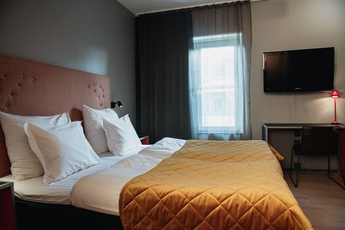 A hotel room with a large bed, a desk, a chair, a flat-screen TV, and a window with curtains.