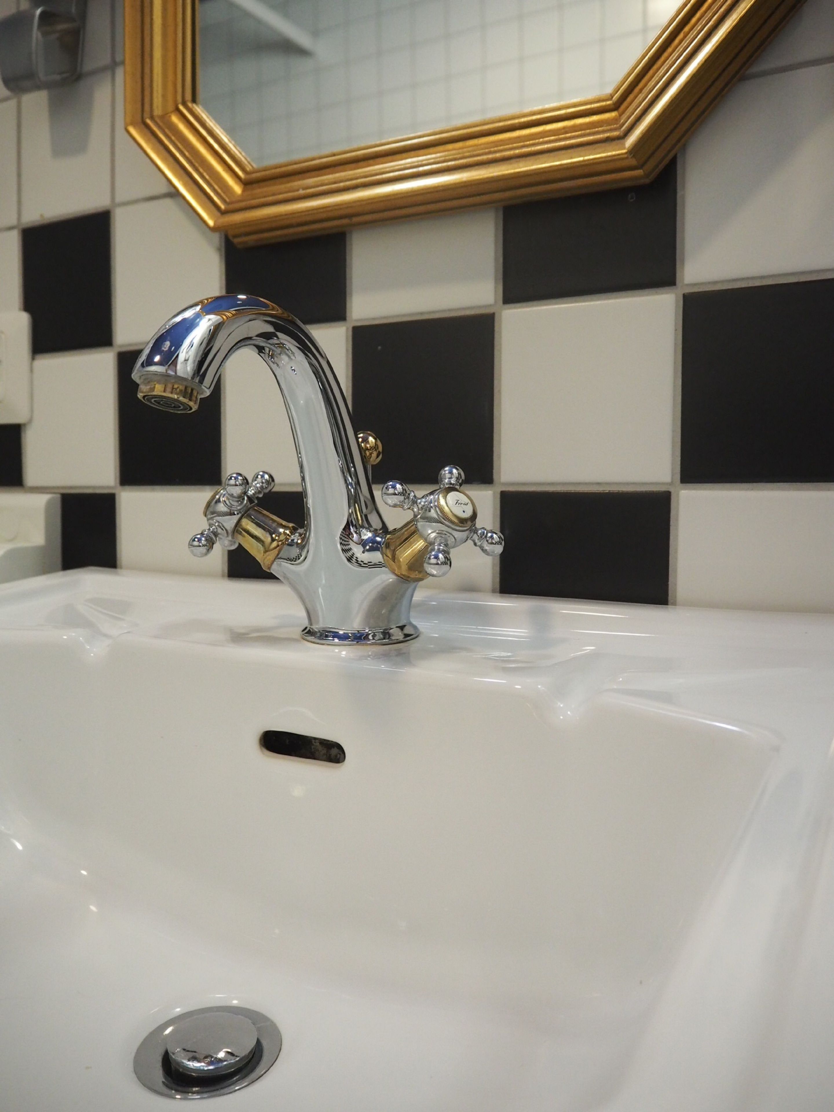 Een wastafel met een chromen kraan en een zeepdispenser in goudkleur.