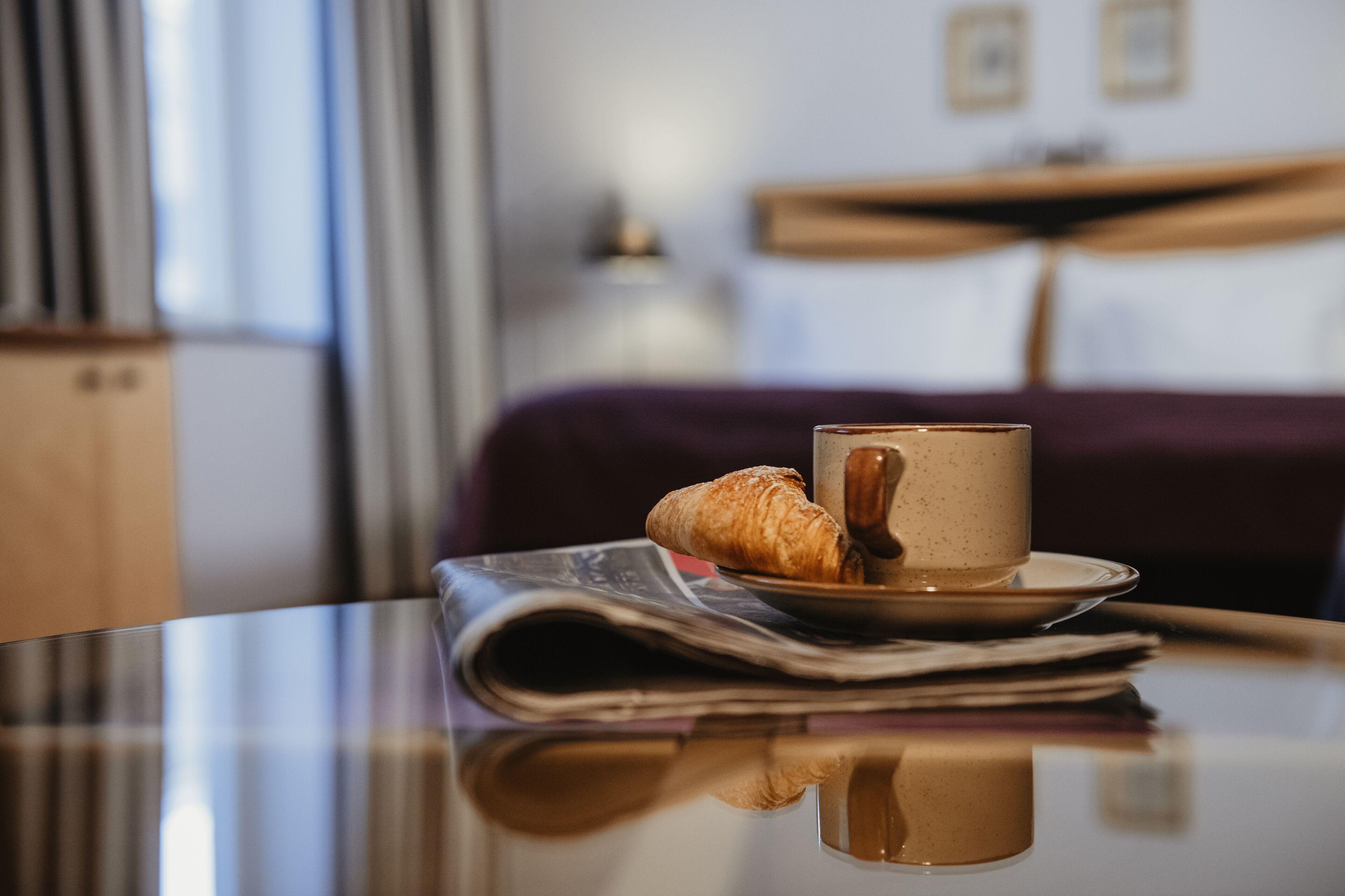 A table with a cup of coffee, a croissant, and a newspaper.