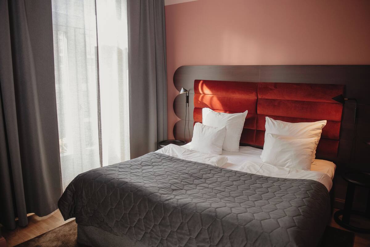A neatly made bed with a grey quilt, a red upholstered headboard, and white pillows.