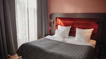 A neatly made bed with a grey quilt, a red upholstered headboard, and white pillows.