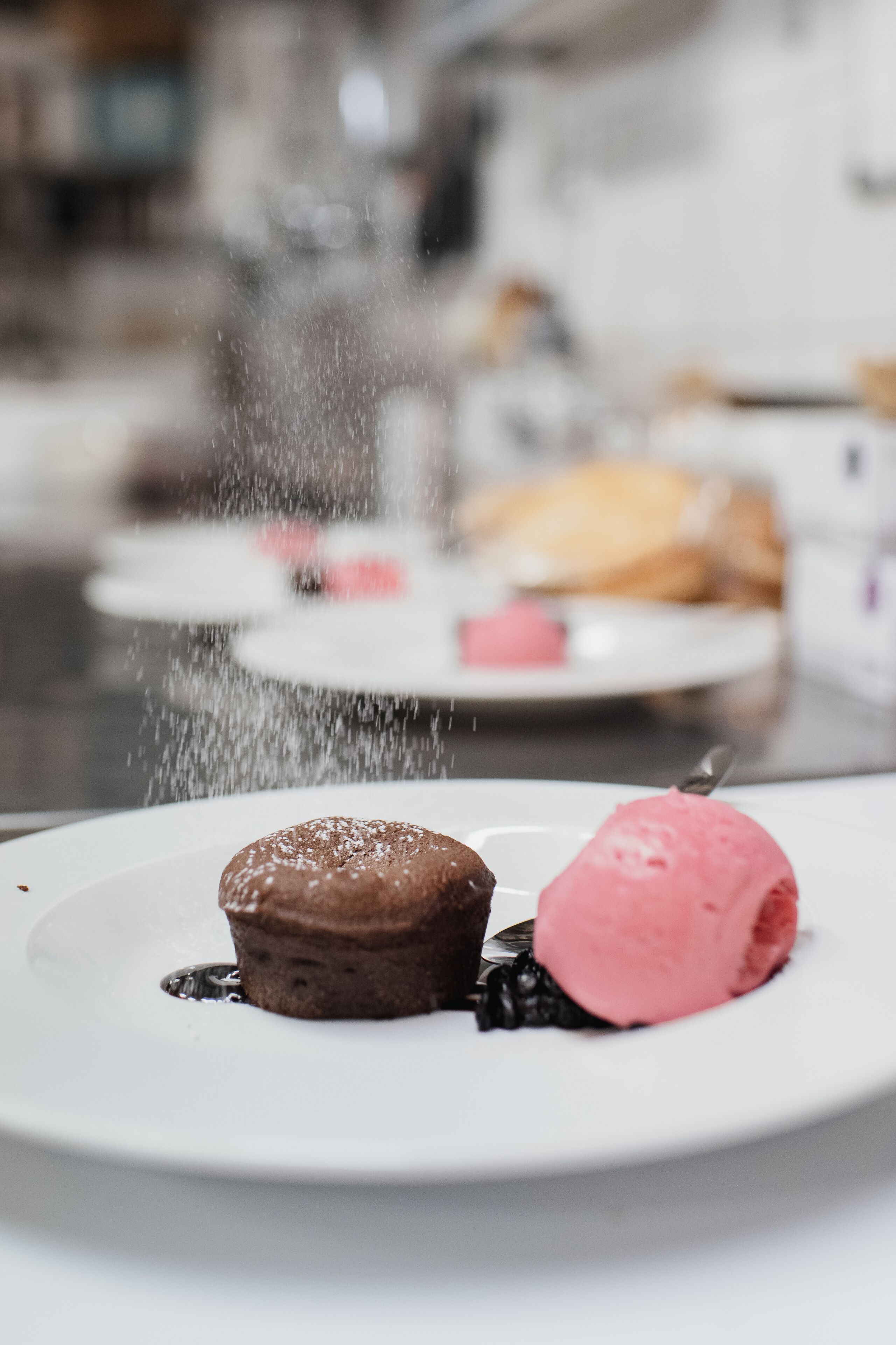 En desserttallrik med en chokladmuffin och en skopa rosa glass, beströdd med florsocker.