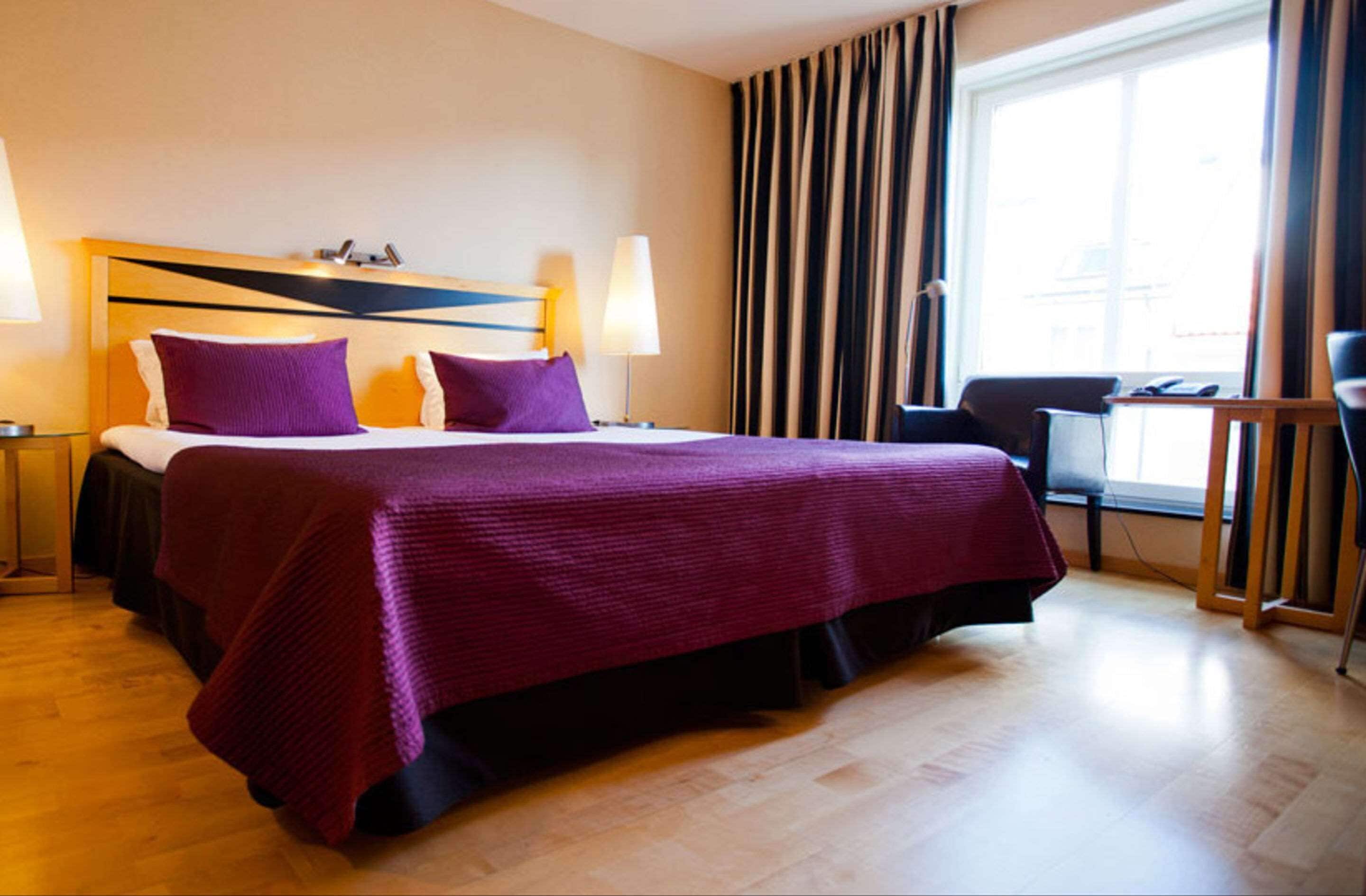A hotel room with a large bed, two bedside lamps, a desk, and a chair.