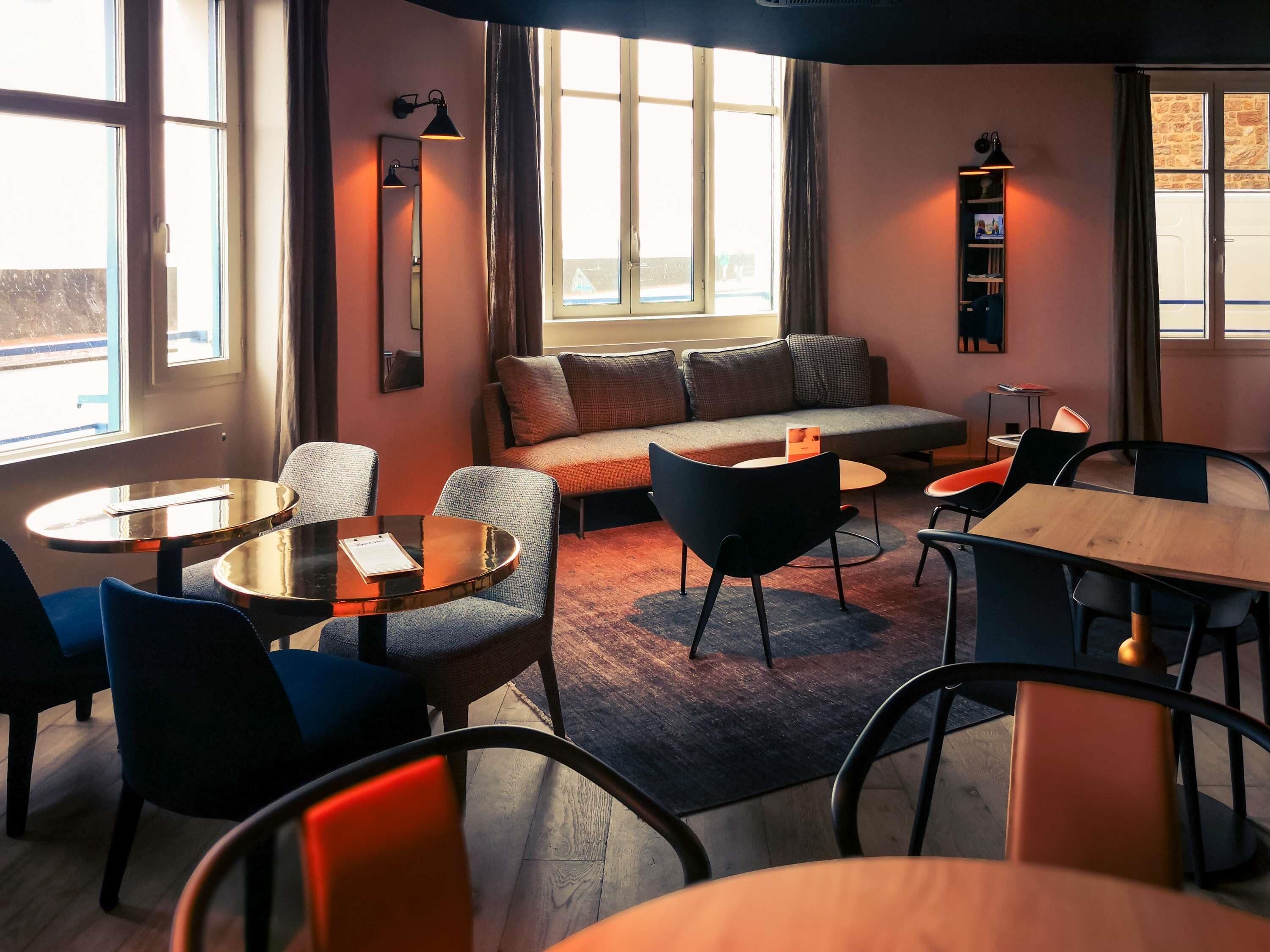 Un intérieur moderne avec un canapé, des tables rondes et des chaises, une bibliothèque et de grandes fenêtres.
