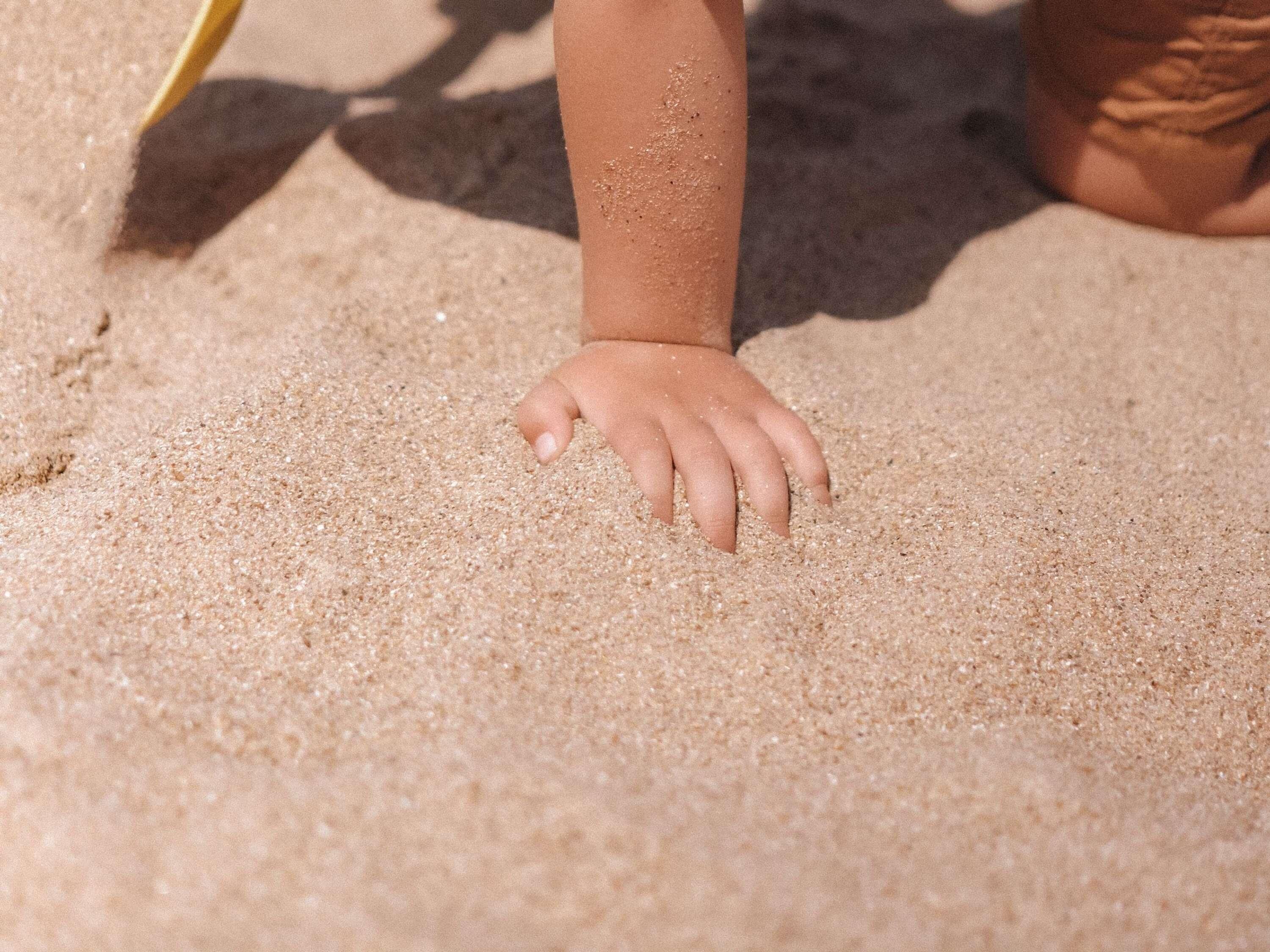 A close-up of a child's hand on sandy ground.