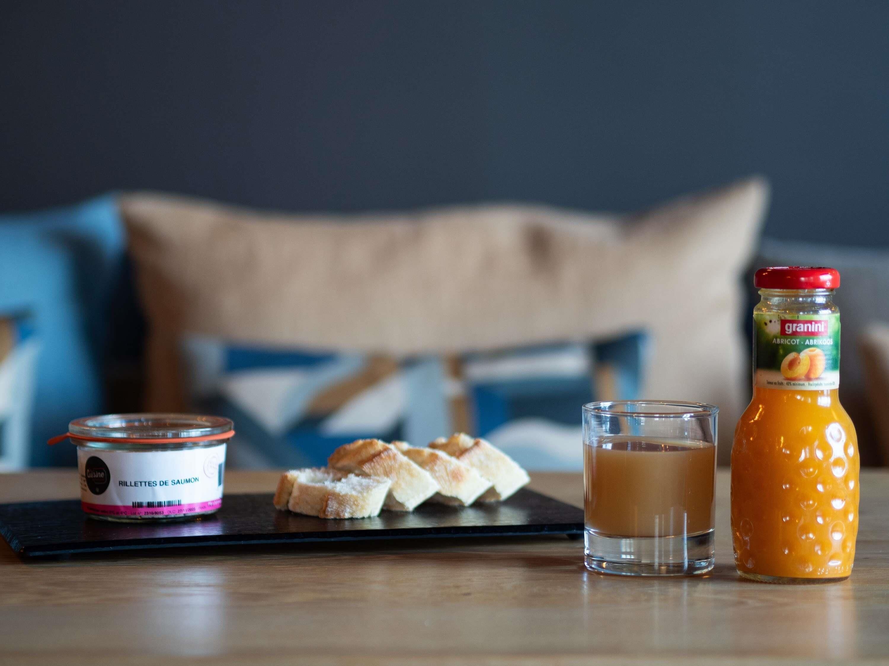 A breakfast setting with a jar of granini apricot, a glass of coffee, and a container of salmon rillettes on a tray.