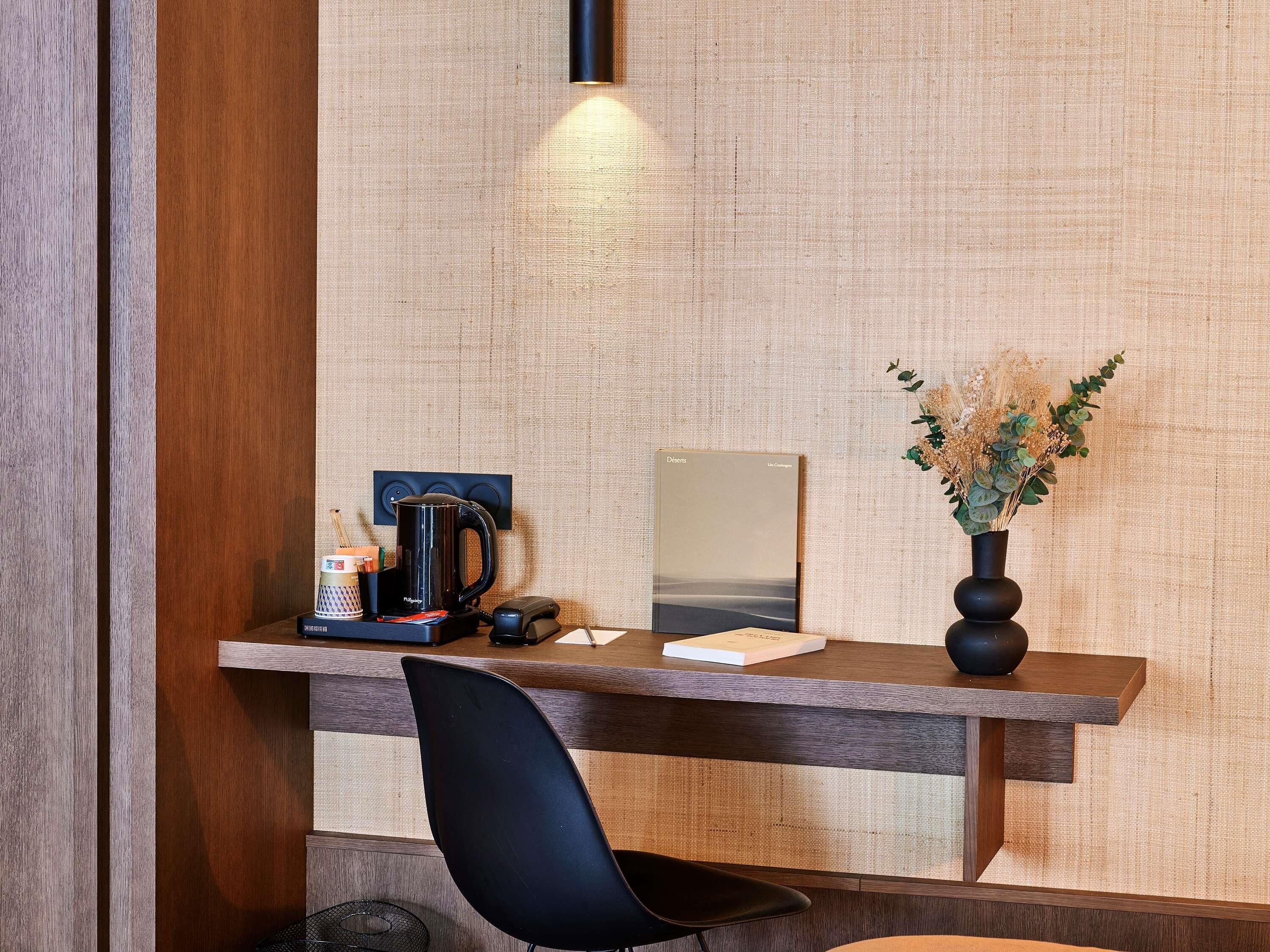 A wooden desk with a black chair, a coffee maker, a phone, and a framed book.