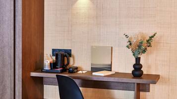 A wooden desk with a black chair, a coffee maker, a phone, and a framed book.
