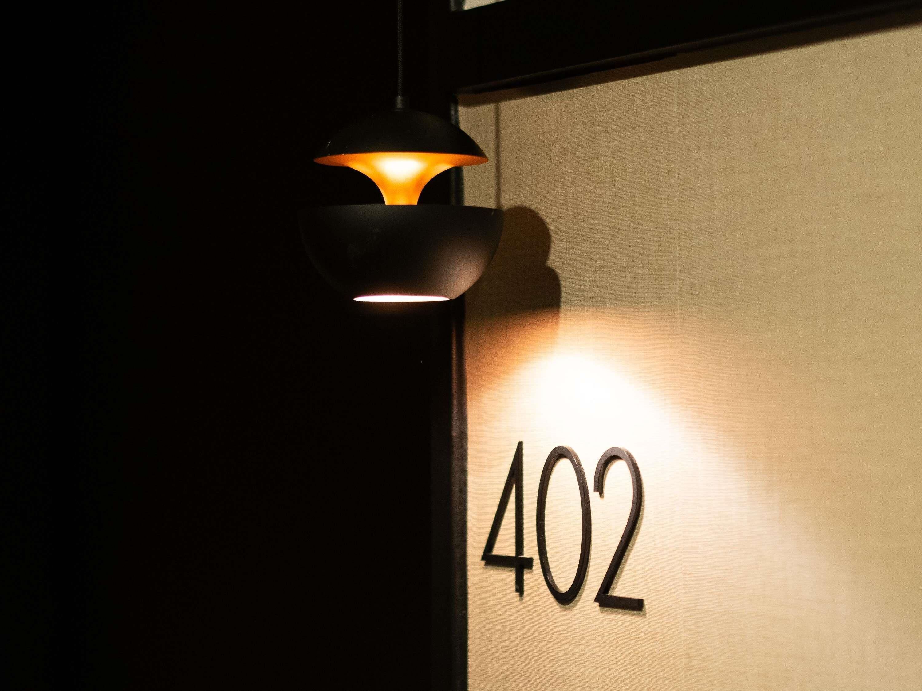Primer plano del número de habitación '402' iluminado por una lámpara fijada a la pared.