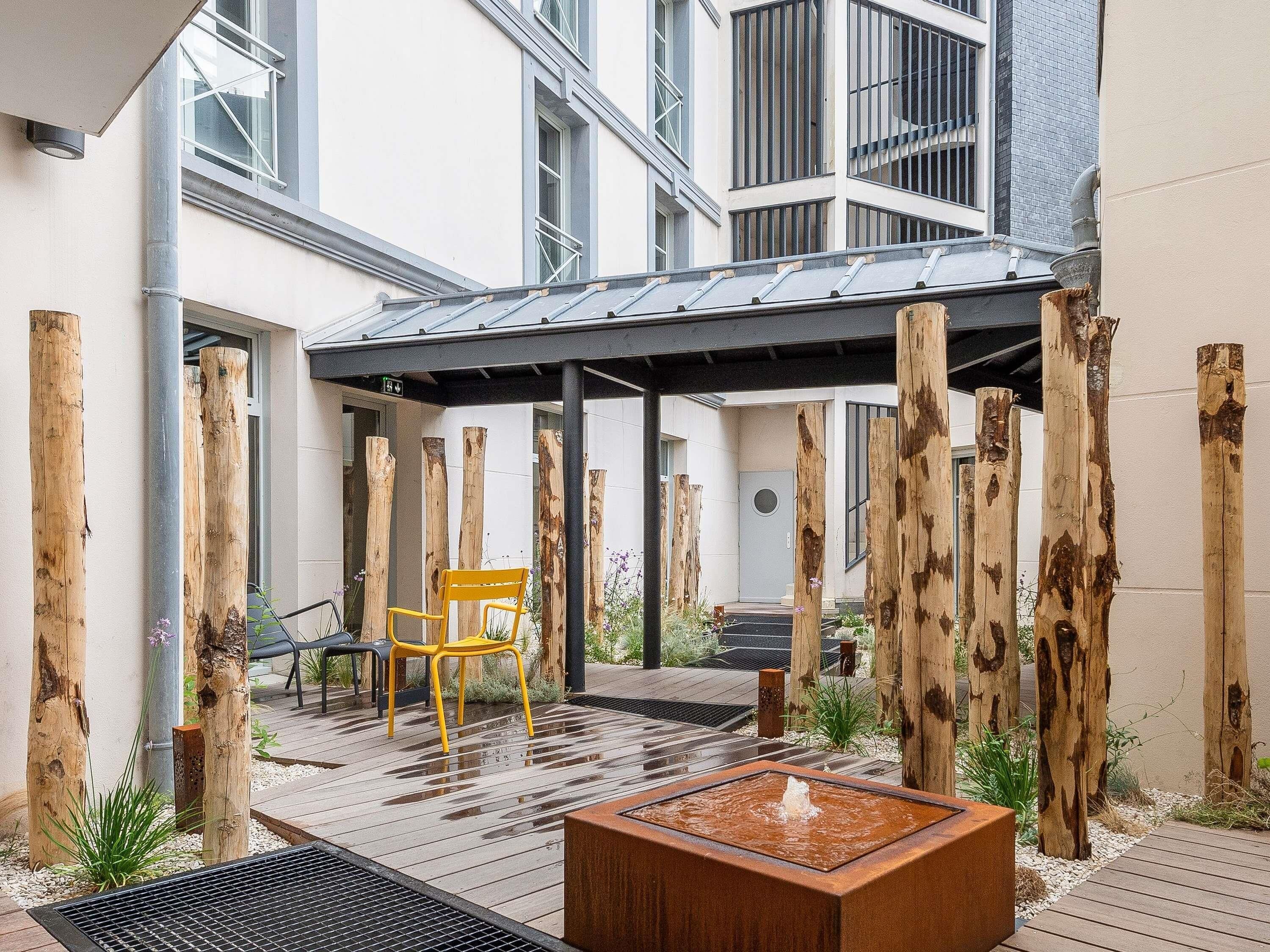 Un patio al aire libre con terraza de madera, una silla amarilla, un elemento acuático y una zona de estar cubierta.