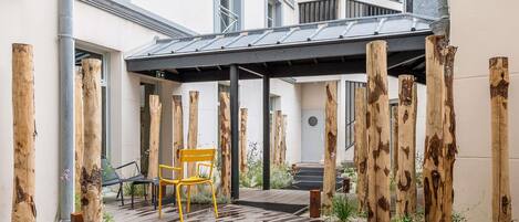 Un espace extérieur aménagé en terrasse, avec un sol en bois, une chaise jaune, un élément décoratif aquatique et un coin salon abrité.