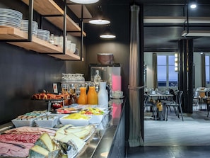 Ein Buffet mit verschiedenen Speisen, eine Kaffeestation und eine Sitzgelegenheit mit Tischen und Stühlen.