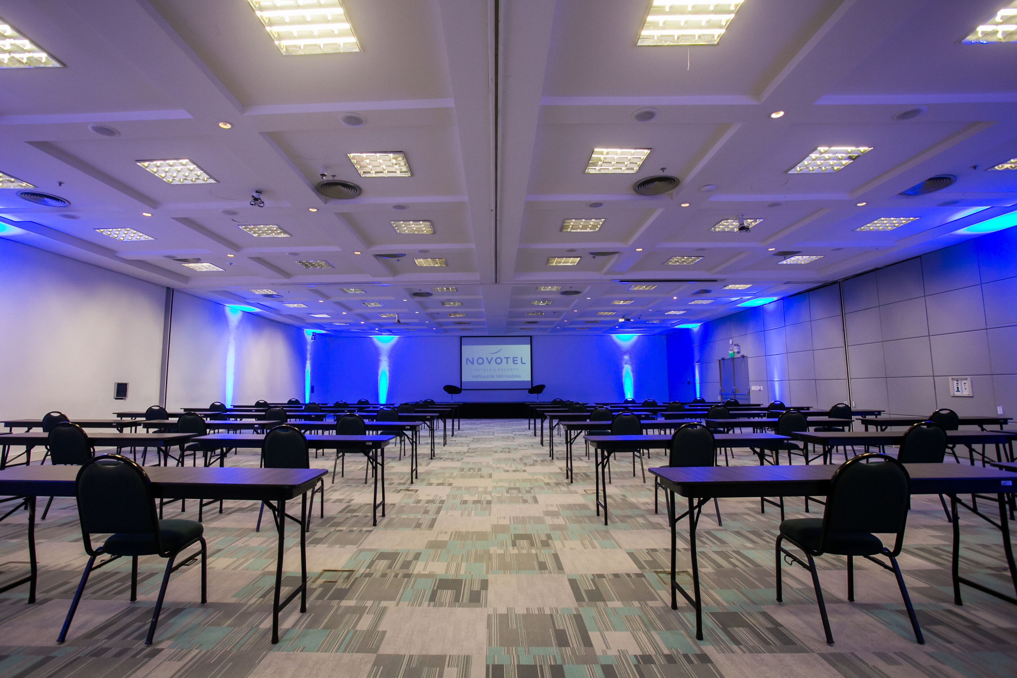 A conference room with tables and chairs, a projector screen, and a stage.