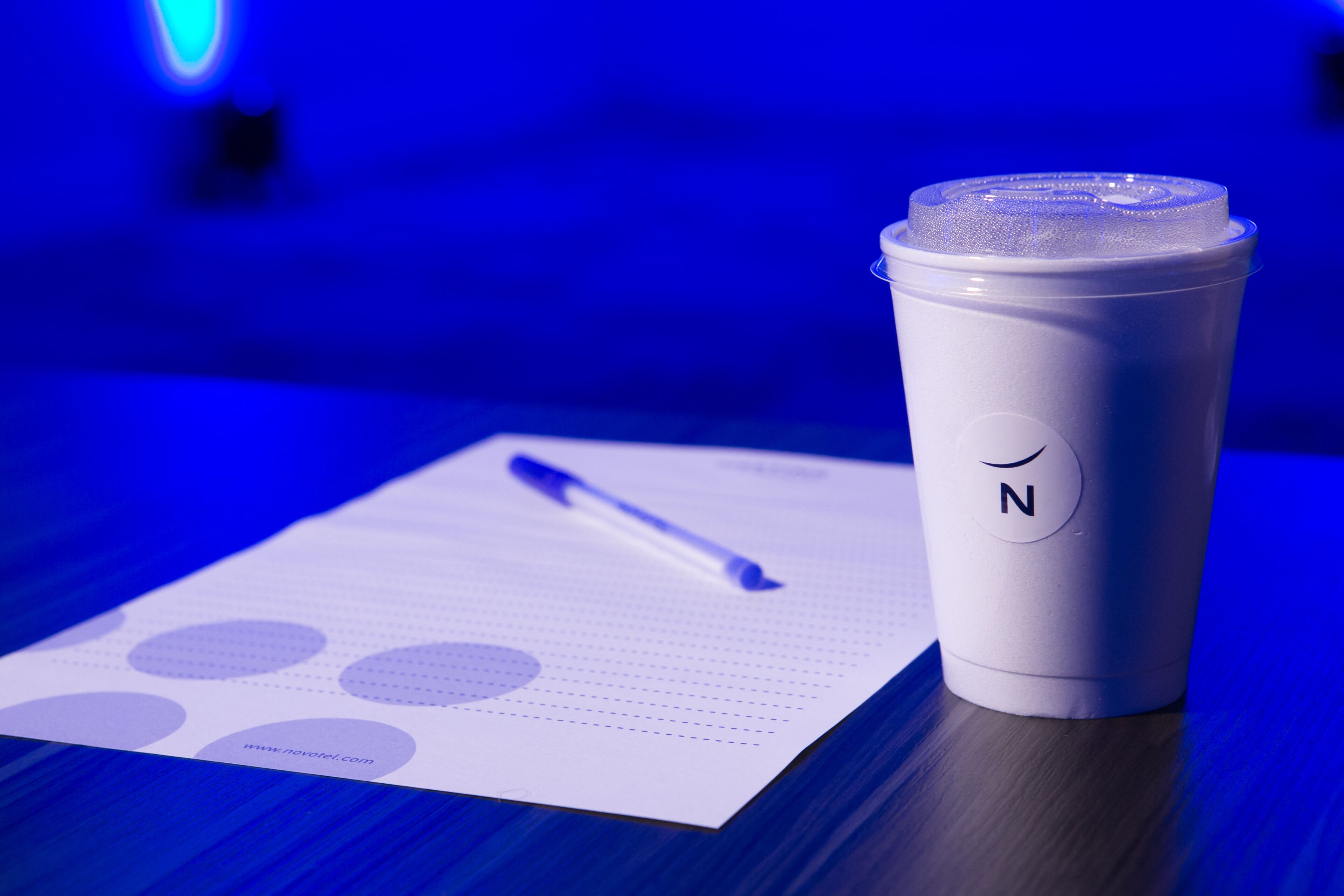 A white cup with a lid and a pen on a piece of paper with dotted lines and circles.