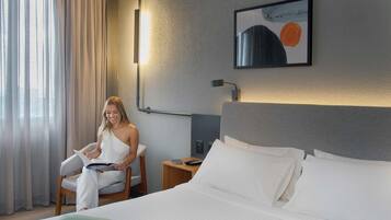 A hotel room with a bed, a chair, a bedside table with a lamp, and a painting on the wall.