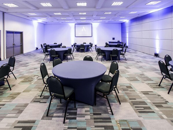 Un salón de conferencias con mesas y sillas redondas, una pantalla de proyector y una alfombra estampada.