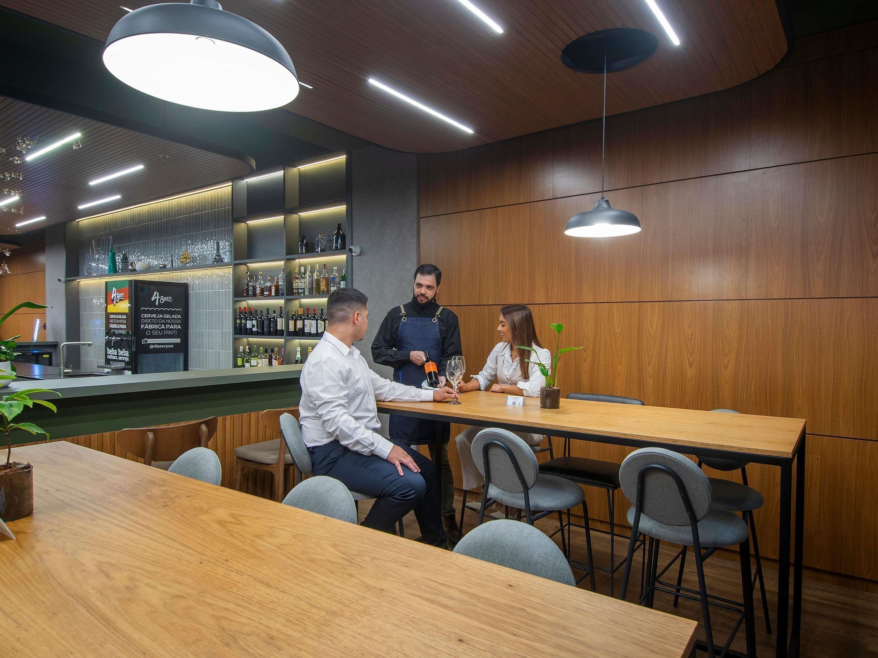 Un bar moderno con paneles de madera, una barra con botellas y una zona de estar con mesas y sillas.